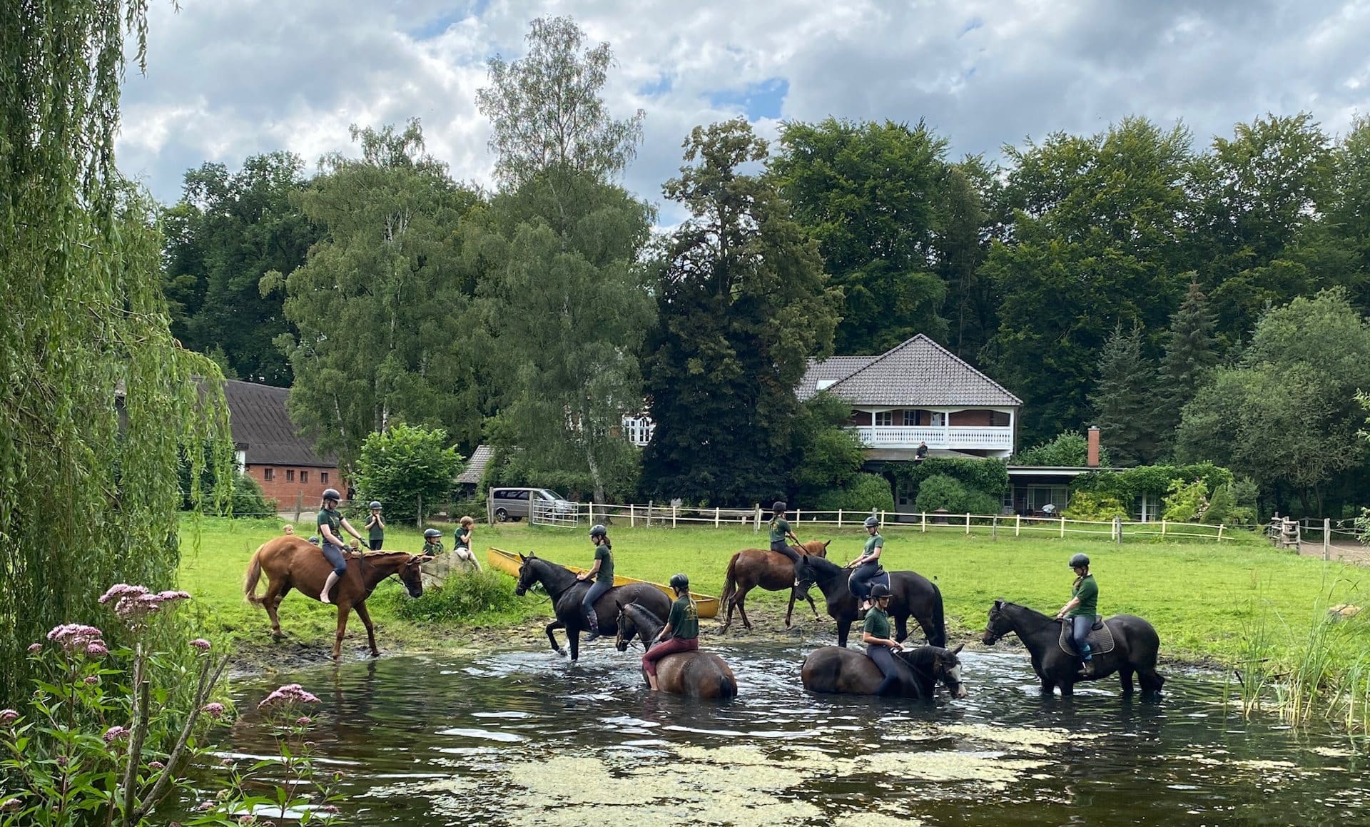 Reitgruppe mit Pferden im Teich vor dem Forsthaus